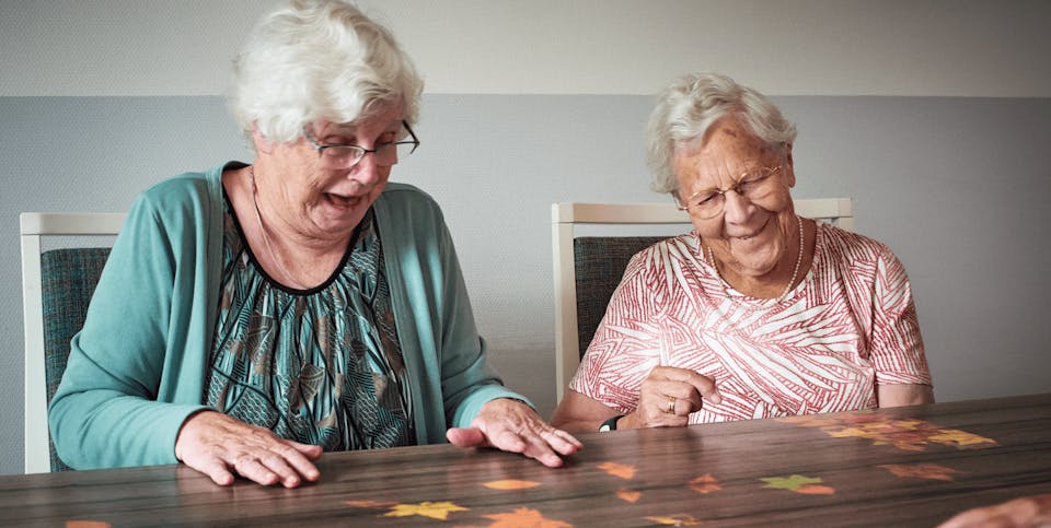 Twee oudere dames met dementie lachen tijdens het spelen met de Tovertafel